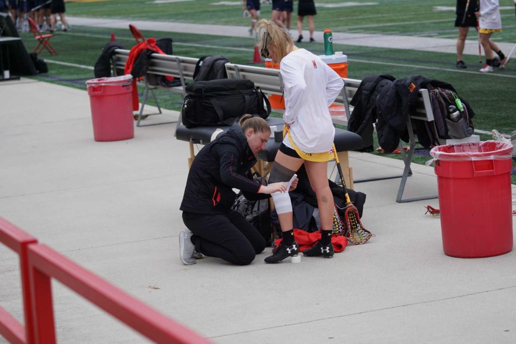Fisioterapia deportiva: mujer atendiendo las lesiones de una atleta en un partido de lacrosse